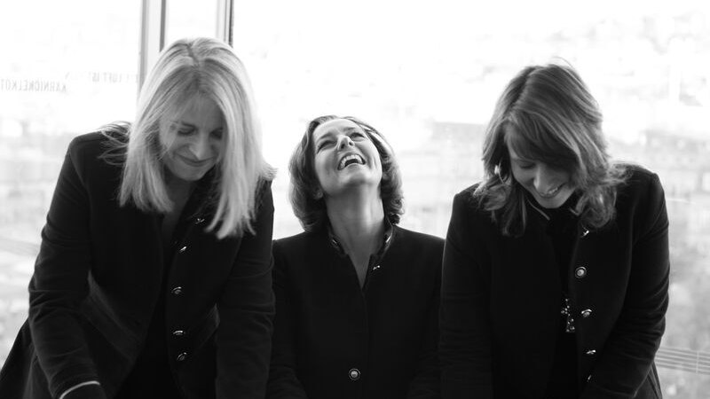 Drei Frauen in Schwarz-Weiß, die lachen und nach unten schauen. Sie tragen dunkle Kleidung und stehen vor einem Fenster., © Theaterhaus Stuttgart e.V. Drei Frauen in Schwarz-Weiß, die lachen und nach unten schauen. Sie tragen dunkle Kleidung und stehen vor einem Fenster., © Theaterhaus Stuttgart e.V.