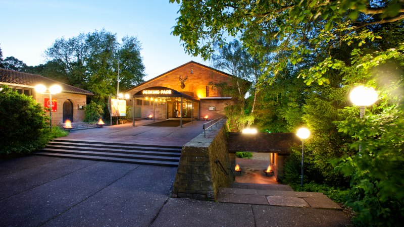 Entrance to Perkins Park in Stuttgart at dusk, surrounded by trees and illuminated with lanterns., © PerkinsPark