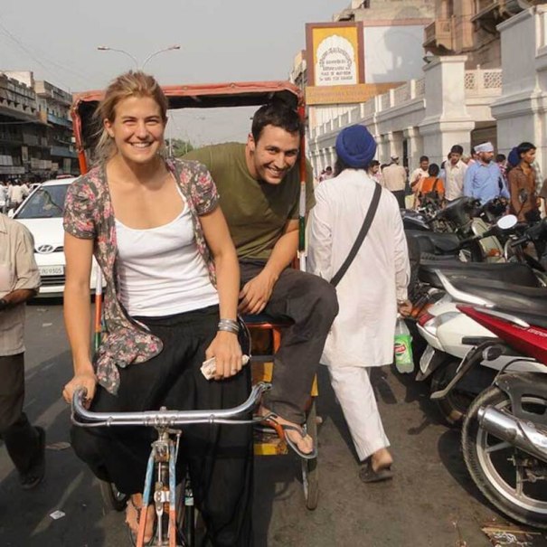 Two people sit happily on a rickshaw in a busy street full of people and motorcycles., © Theaterhaus Stuttgart e.V. Two people sit happily on a rickshaw in a busy street full of people and motorcycles., © Theaterhaus Stuttgart e.V.