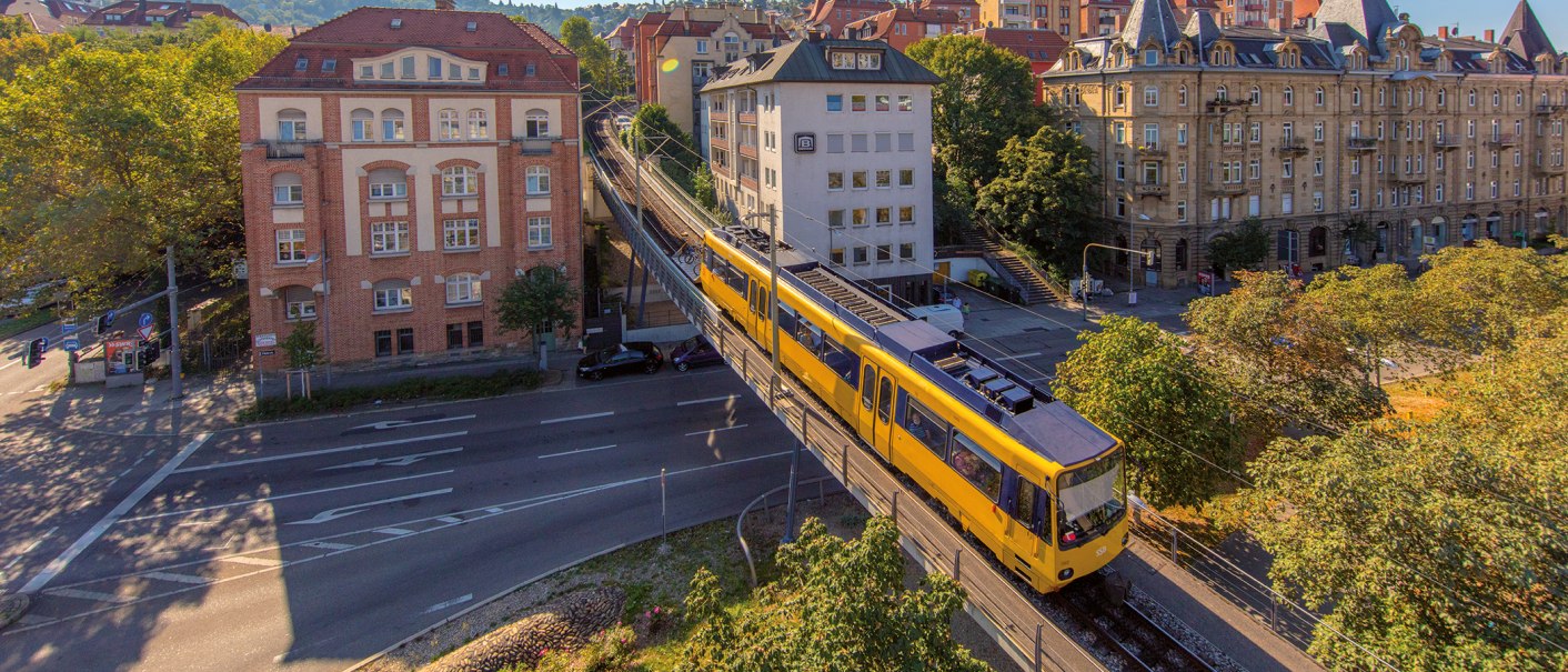 The cog railroad in Stuttgart runs on an elevated track through an urban environment with historic buildings and trees., © SMG, Achim Mende The cog railroad in Stuttgart runs on an elevated track through an urban environment with historic buildings and trees., © SMG, Achim Mende