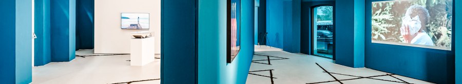 Modern gallery with blue walls, video installations and geometric patterns on the floor. Industrial design with visible ventilation pipes., &copy; Publication only by client - disclosure to third parties only after consultation.