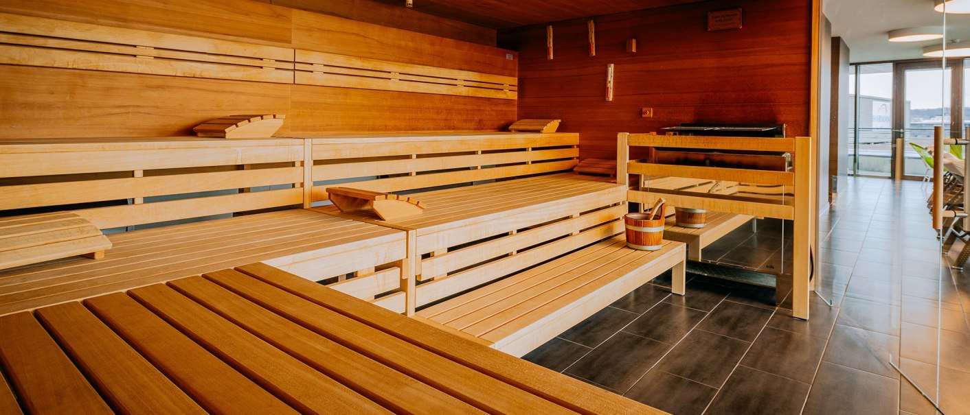 Moderne Sauna mit Holzbänken, einem Eimer und einem Fenster mit Blick nach draußen. Entspannte Atmosphäre im Spa-Bereich., © V8 HOTEL
