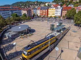 Luftaufnahme des Marienplatzes in Stuttgart. Eine gelbe Stra&szlig;enbahn f&auml;hrt vorbei, umgeben von B&auml;umen und Geb&auml;uden. Der Platz ist belebt und sonnig., &copy; Stuttgart-Marketing GmbH, Achim Mende