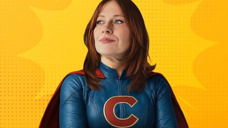 Frau in blauem Superheldenkostüm mit rotem Umhang und "C" auf der Brust vor gelbem Comic-Hintergrund., © Theaterhaus Stuttgart e.V. Frau in blauem Superheldenkostüm mit rotem Umhang und "C" auf der Brust vor gelbem Comic-Hintergrund., © Theaterhaus Stuttgart e.V.