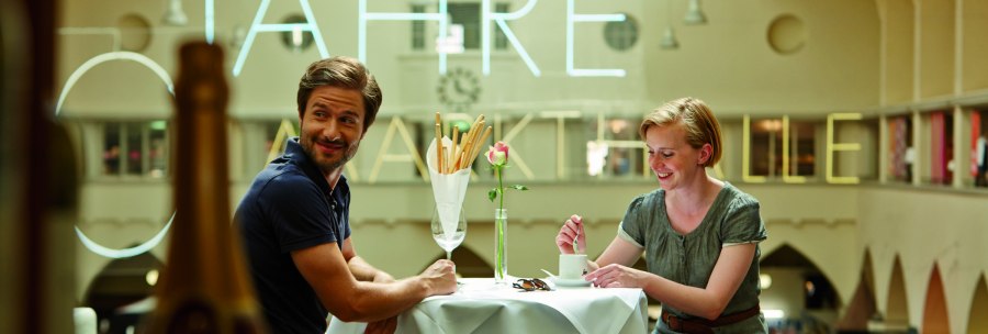 Ein Paar sitzt l&auml;chelnd an einem Tisch in einem Caf&eacute;. Im Hintergrund sind gro&szlig;e Buchstaben an der Wand sichtbar., &copy; TMBW, Christoph D&uuml;pper