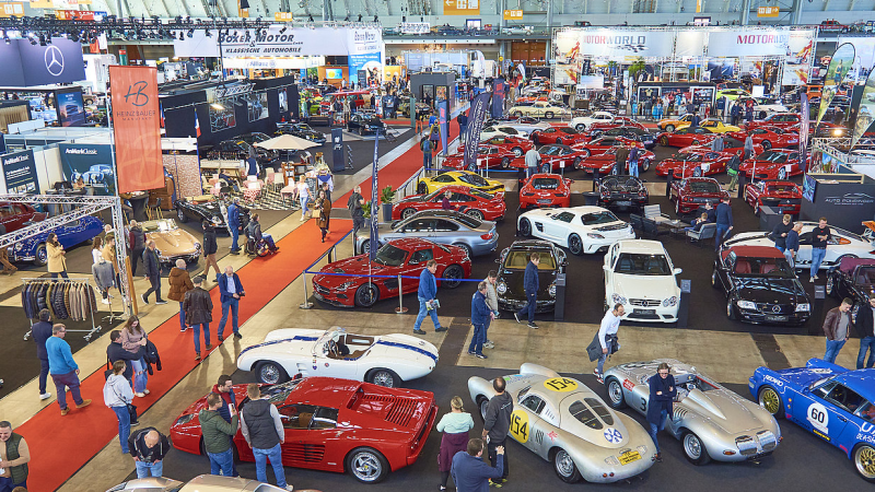 Vogelperspektive auf eine Automesse mit vielen klassischen und modernen Autos, Ständen und Besuchern. Markenlogos und rote Teppiche sind sichtbar., © RETRO CLASSICS® Vogelperspektive auf eine Automesse mit vielen klassischen und modernen Autos, Ständen und Besuchern. Markenlogos und rote Teppiche sind sichtbar., © RETRO CLASSICS®