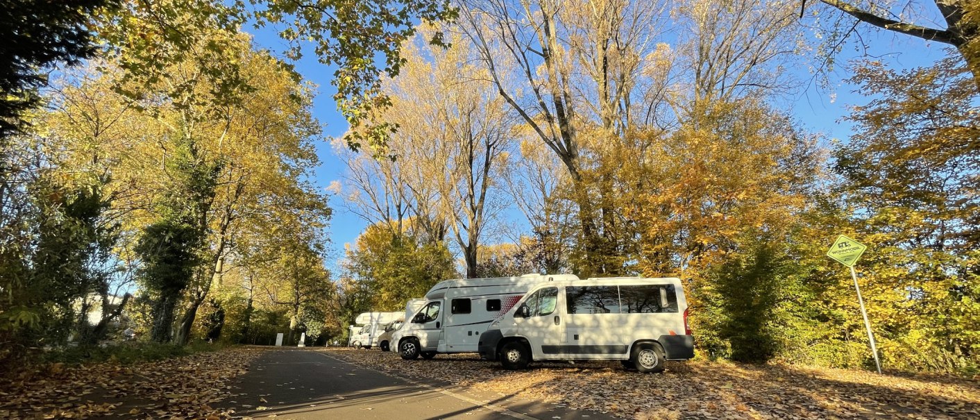 Wohnmobile parken auf einem herbstlichen Stellplatz, umgeben von bunten B&auml;umen und Laub. Ein Schild weist auf den Wohnmobilstellplatz hin., &copy; Stadtmarketing G&ouml;ppingen