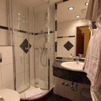 Modernes Badezimmer mit Glasdusche, Waschbecken und Handtuchhalter. Weiße Fliesen mit schwarzen Akzenten. Beleuchtung an der Decke., © Aparthotel Astro Modernes Badezimmer mit Glasdusche, Waschbecken und Handtuchhalter. Weiße Fliesen mit schwarzen Akzenten. Beleuchtung an der Decke., © Aparthotel Astro