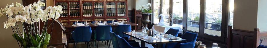 Elegant restaurant with blue chairs, wooden floor and large windows. Orchids and a display case with bottles decorate the room., © Steigenberger Hotels GmbH