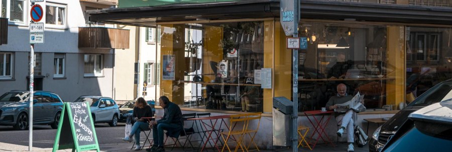 Ein Caf&eacute; namens Kantinchen mit gelbem und gr&uuml;nem Schild. Drau&szlig;en sitzen Menschen an bunten Tischen. Verkehrsschilder und Autos sind zu sehen., &copy; SMG, Sarah Schmid