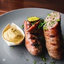 Grilled sausages on a plate with mustard and gherkin slices, garnished with herbs., &copy; links im Bild
