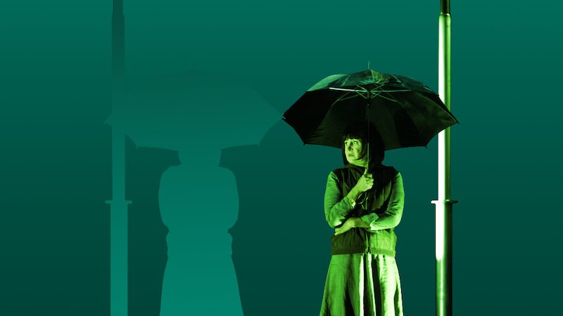 Person mit Regenschirm unter Stra&szlig;enlaterne, daneben Silhouette. Gr&uuml;ner Hintergrund, thematisiert Klimakrise., &copy; Theater der Altstadt