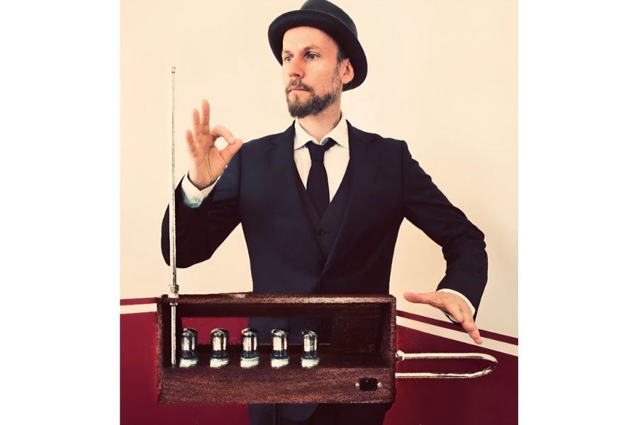 Ein Mann im Anzug und Hut spielt ein Theremin, ein elektronisches Musikinstrument, mit Gesten der Hände in der Luft., © Fotocredit Theater La Lune Stuttgart
