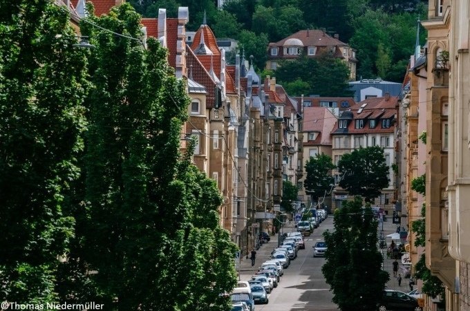 Straße in Stuttgart mit historischen Gebäuden, Bäumen und parkenden Autos. Im Hintergrund sind grüne Hügel und weitere Häuser zu sehen., © Stuttgart Marketing GmbH Straße in Stuttgart mit historischen Gebäuden, Bäumen und parkenden Autos. Im Hintergrund sind grüne Hügel und weitere Häuser zu sehen., © Stuttgart Marketing GmbH