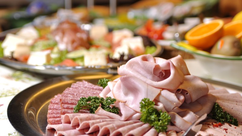 Ein Teller mit verschiedenen Wurstsorten, darunter Schinken und Salami, dekoriert mit Petersilie. Im Hintergrund sind weitere Speisen zu sehen., © TOMAS Ein Teller mit verschiedenen Wurstsorten, darunter Schinken und Salami, dekoriert mit Petersilie. Im Hintergrund sind weitere Speisen zu sehen., © TOMAS