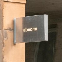 Ein Metallschild mit der Aufschrift 'abnorm' hängt an einer Wand. Daneben ist ein Kunstplakat zu sehen., © SMG, Sarah Schmid Ein Metallschild mit der Aufschrift 'abnorm' hängt an einer Wand. Daneben ist ein Kunstplakat zu sehen., © SMG, Sarah Schmid