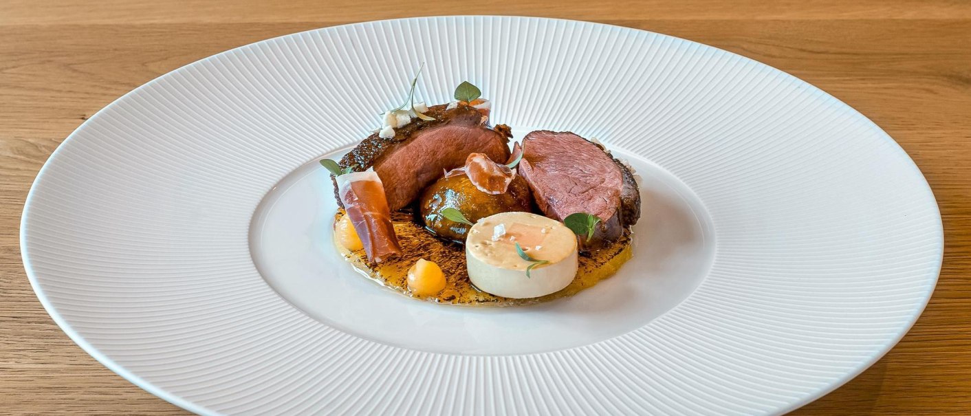 Gourmetgericht mit Entenbrust, dekorativ angerichtet auf einem wei&szlig;en Teller. Beilagen und So&szlig;en kunstvoll platziert, auf einem Holztisch serviert., &copy; New Josch, Stuttgart