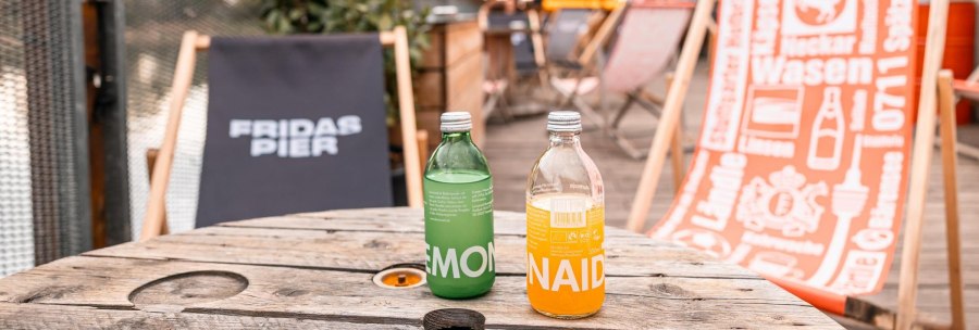 Two bottles of lemonade on a wooden table, surrounded by deckchairs at Frida's pier. Relaxed atmosphere outdoors., © SMG Stuttgart Marketing GmbH - Sarah Schmid Two bottles of lemonade on a wooden table, surrounded by deckchairs at Frida's pier. Relaxed atmosphere outdoors., © SMG Stuttgart Marketing GmbH - Sarah Schmid