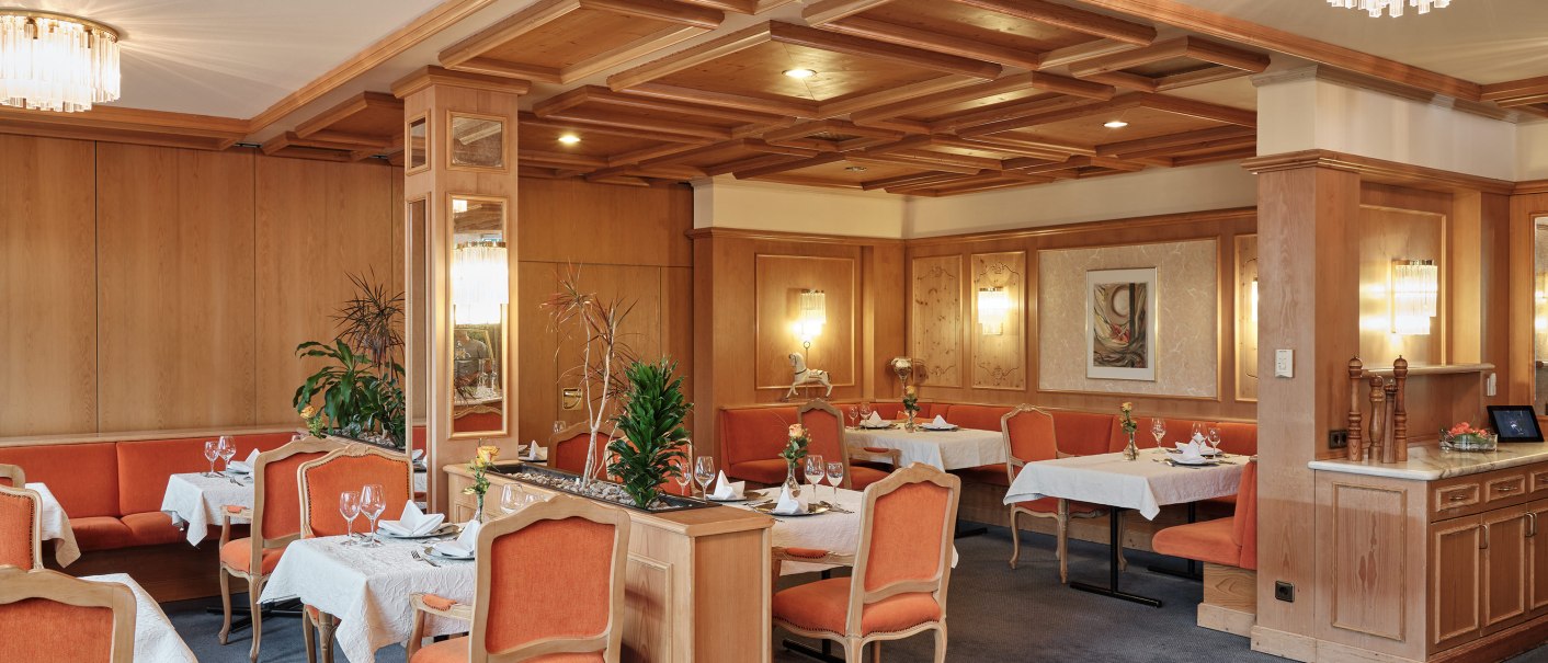 Elegantes Restaurant mit Holzeinrichtung, orangefarbenen Stühlen und weiß gedeckten Tischen. Dezente Beleuchtung und Pflanzen sorgen für eine gemütliche Atmosphäre., © Badhotel Restaurant Stauferland
