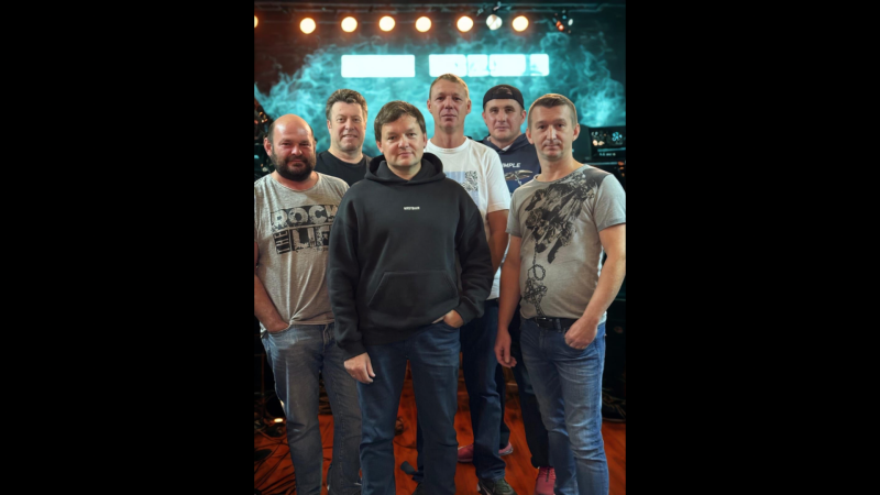 Sechs Männer in Freizeitkleidung posieren vor einer Bühne mit Lichtern und Rauch im Hintergrund., © Sowerscheno Sekretno Sechs Männer in Freizeitkleidung posieren vor einer Bühne mit Lichtern und Rauch im Hintergrund., © Sowerscheno Sekretno