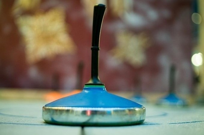 Nahaufnahme eines blauen Eisstocks auf einer Eisbahn, unscharfer Hintergrund mit winterlichen Dekorationen., © Cool-Tours StattReisen Nahaufnahme eines blauen Eisstocks auf einer Eisbahn, unscharfer Hintergrund mit winterlichen Dekorationen., © Cool-Tours StattReisen