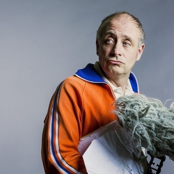 Ein Mann in einem orangefarbenen Trainingsanzug mit blauem Kragen hält ein Mikrofon mit Windschutz., © Theaterhaus Stuttgart e.V.
