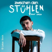 Ein Mann lehnt sich auf einen Stuhl vor blauem Hintergrund. Text: 'Zwischen den Stühlen Tour 2026'., © links im Bild Ein Mann lehnt sich auf einen Stuhl vor blauem Hintergrund. Text: 'Zwischen den Stühlen Tour 2026'., © links im Bild