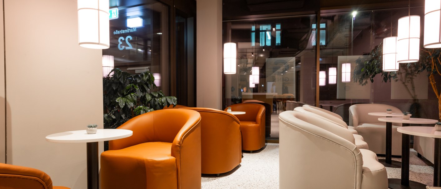 Moderne Lounge mit orangefarbenen und weißen Sesseln, runden Tischen und Hängelampen. Große Fenster und Pflanzen schaffen eine einladende Atmosphäre., © GINN Apartments Esslingen Moderne Lounge mit orangefarbenen und weißen Sesseln, runden Tischen und Hängelampen. Große Fenster und Pflanzen schaffen eine einladende Atmosphäre., © GINN Apartments Esslingen