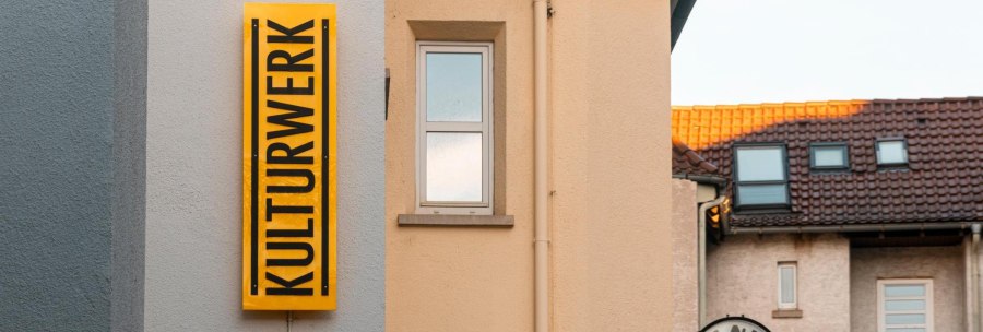 A yellow sign with the inscription 'KULTURWERK' hangs on the wall of a house. Next to it is a window and a clock., &copy; SMG Stuttgart Marketing GmbH - Sarah Schmid