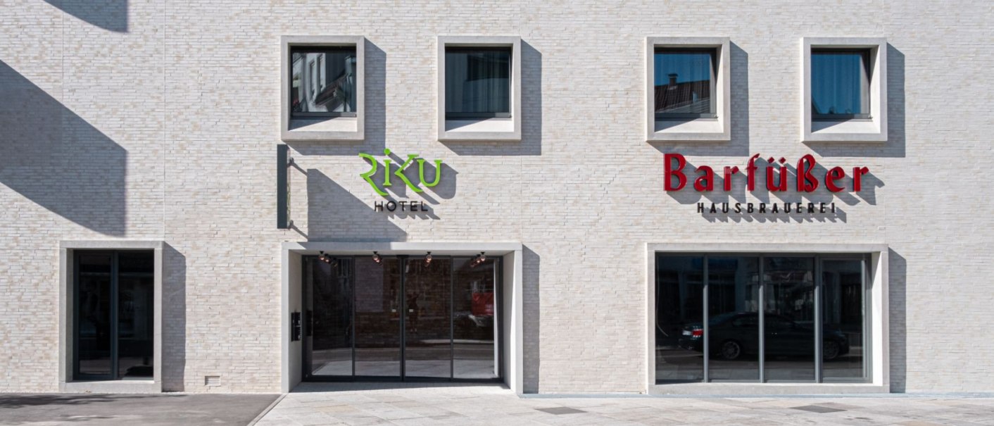 Moderne Fassade mit Schildern von Riku Hotel und Barf&uuml;&szlig;er Hausbrauerei, helle Ziegelsteine, gro&szlig;e Fenster., &copy; 13 6 Design GmbH (Judenhof 10, 89073 Ulm)