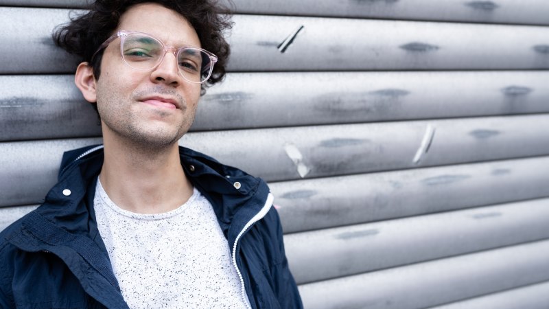 Ein Mann mit lockigem Haar und Brille lehnt l&auml;ssig an einer grauen, metallischen Wand., &copy; Julia Sch&auml;fer