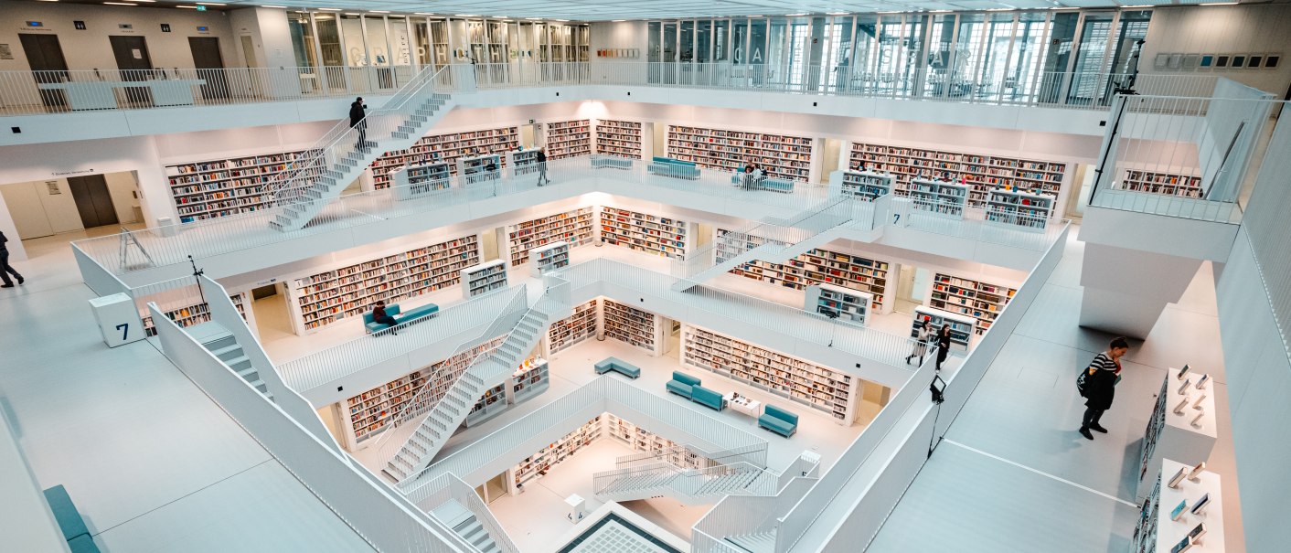 Moderne, helle Bibliothek mit mehreren Etagen, weißen Wänden und Bücherregalen. Menschen bewegen sich auf den Treppen und lesen Bücher., © Stuttgart-Marketing GmbH, Sarah Schmid