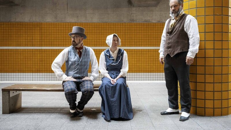 Drei Personen in historischer Kleidung sitzen und stehen in einer modernen Umgebung mit gelben Fliesen und Betonw&auml;nden., &copy; Rosenau Kultur e.V.