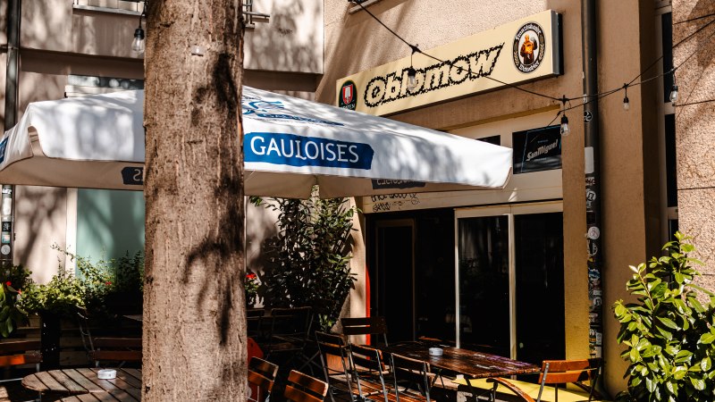 Außenbereich eines Cafés namens Oblomow mit Holztischen, Stühlen und einem Gauloises-Sonnenschirm. Ein Baum steht im Vordergrund., © SMG_Sarah Schmid Außenbereich eines Cafés namens Oblomow mit Holztischen, Stühlen und einem Gauloises-Sonnenschirm. Ein Baum steht im Vordergrund., © SMG_Sarah Schmid