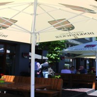 Outdoor area of the Dinkelacker brewery restaurant with wooden benches and parasols. Guests sit in the shade and enjoy the weather., © © Stuttgart-Marketing GmbH (SMG)