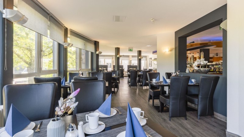 Modern breakfast area with laid tables, blue napkins and large windows that let in plenty of light., © Plaza INN Stuttgart-Filderstadt Modern breakfast area with laid tables, blue napkins and large windows that let in plenty of light., © Plaza INN Stuttgart-Filderstadt