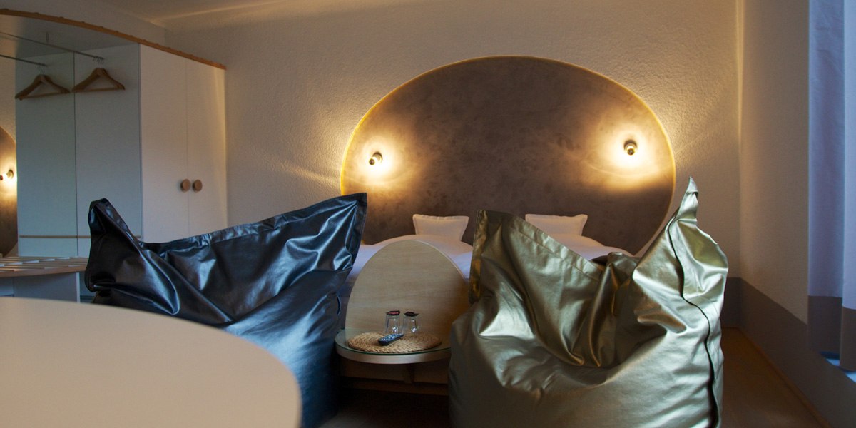 Modernes Doppelzimmer mit zwei Sitzsäcken, einem runden Tisch und einem beleuchteten Kopfteil am Bett., © Hotelmärchen Modernes Doppelzimmer mit zwei Sitzsäcken, einem runden Tisch und einem beleuchteten Kopfteil am Bett., © Hotelmärchen