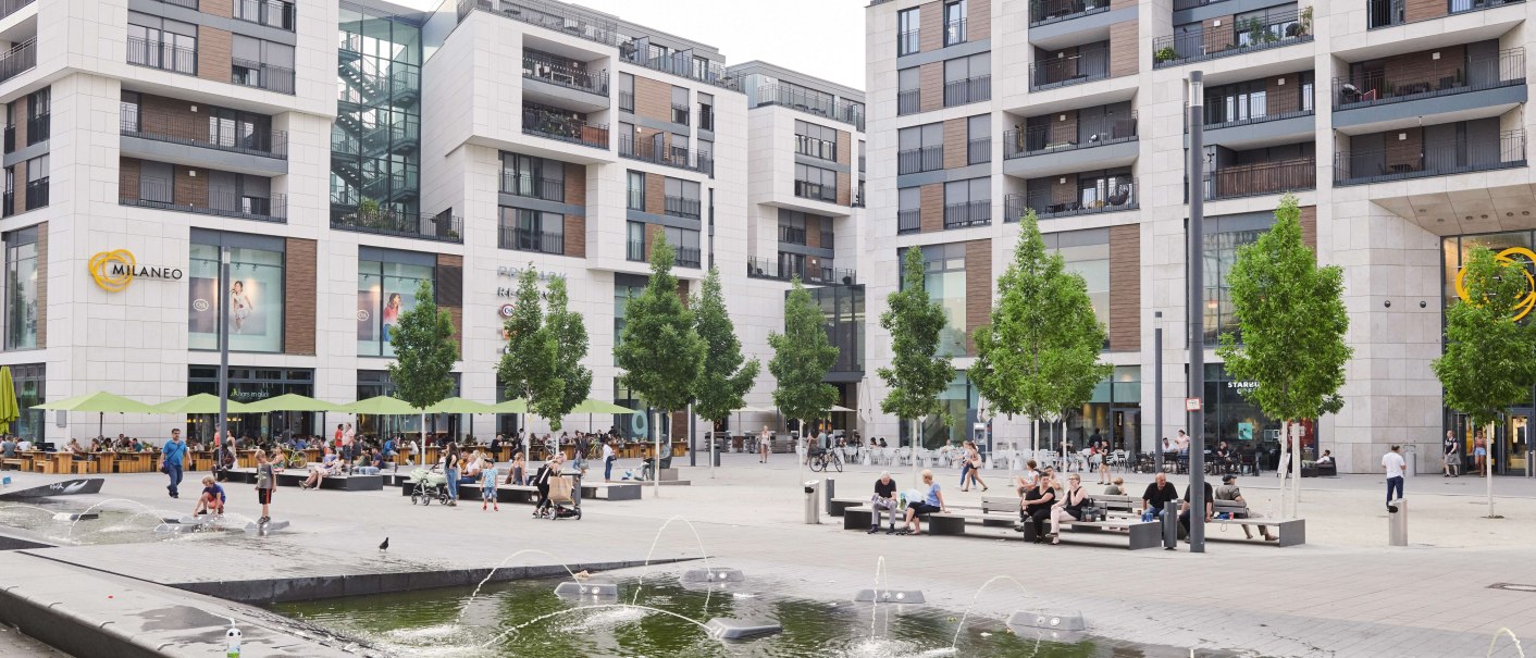 The Milaneo shopping center on Mail&auml;nder Platz with modern buildings, trees and a fountain in the foreground. People sit and walk., &copy; Peter Oppenl&auml;nder