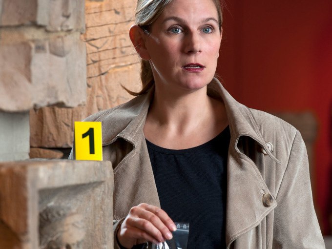 A woman in a beige coat holds a piece of evidence in the museum. A yellow mark with the number 1 can be seen next to her., © Landesmuseum Württemberg A woman in a beige coat holds a piece of evidence in the museum. A yellow mark with the number 1 can be seen next to her., © Landesmuseum Württemberg