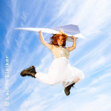 Eine Person springt mit einem großen Papierflugzeug in der Hand vor einem blauen Himmel mit weißen Wolken., © links im Bild