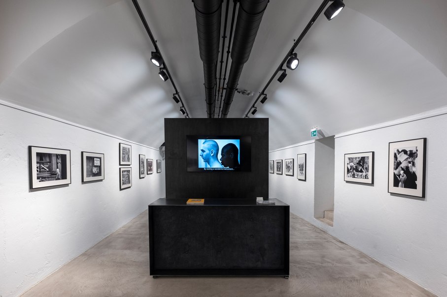 Galerie mit weißen Wänden, Fotografien in Schwarz-Weiß und einem zentralen Bildschirm. Moderne Beleuchtung und ein minimalistisches Design., © Holger Strehlow