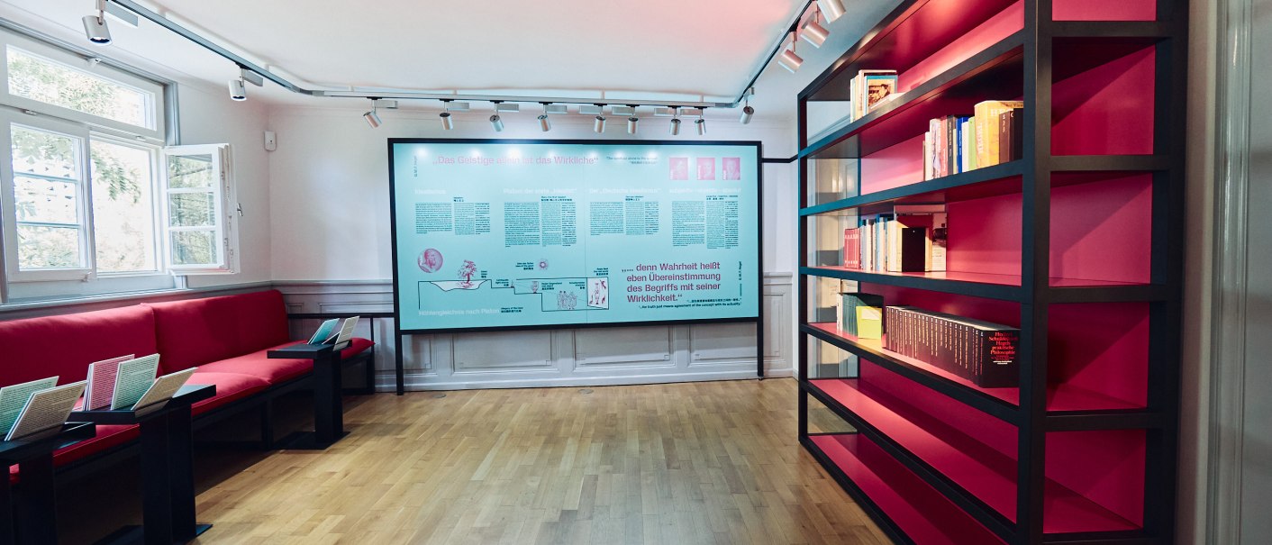 Hegel-Haus Dauerausstellung: Raum mit roten Sitzbänken, einem großen Bücherregal und einer Infotafel an der Wand. Helle, moderne Einrichtung., © Julia Ochs Hegel-Haus Dauerausstellung: Raum mit roten Sitzbänken, einem großen Bücherregal und einer Infotafel an der Wand. Helle, moderne Einrichtung., © Julia Ochs