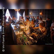 A group of people sit at a stylish bar and take part in a cocktail tasting. The atmosphere is cozy and convivial., &copy; links im Bild