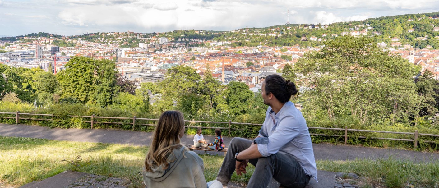 Zwei Personen sitzen auf einer Wiese und schauen auf die Stadt Stuttgart. Im Hintergrund sind H&uuml;gel und Geb&auml;ude zu sehen, darunter der Fernsehturm., &copy; SMG, Martina Denker