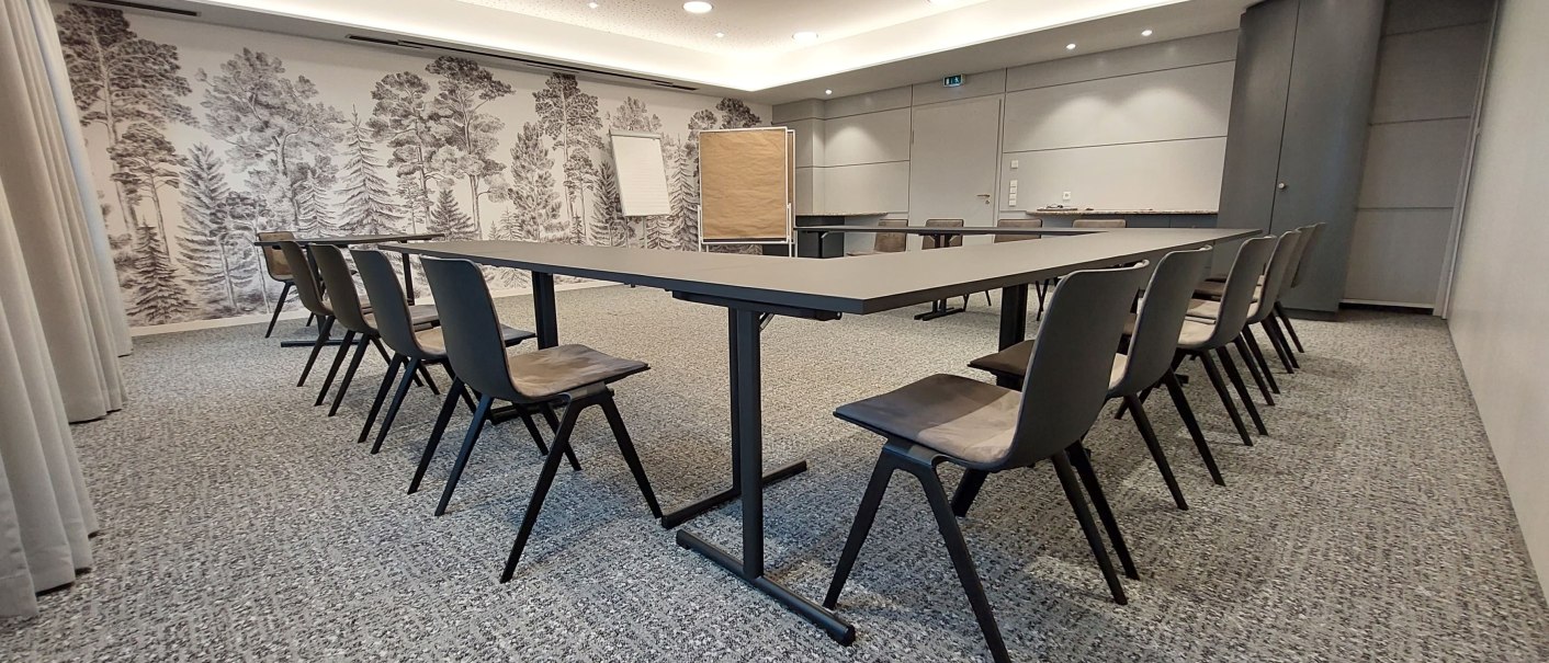 A modern meeting room with a U-shaped table arrangement, gray chairs and a wall with forest wallpaper. Flipchart and projector are available., © Erikson Hotel