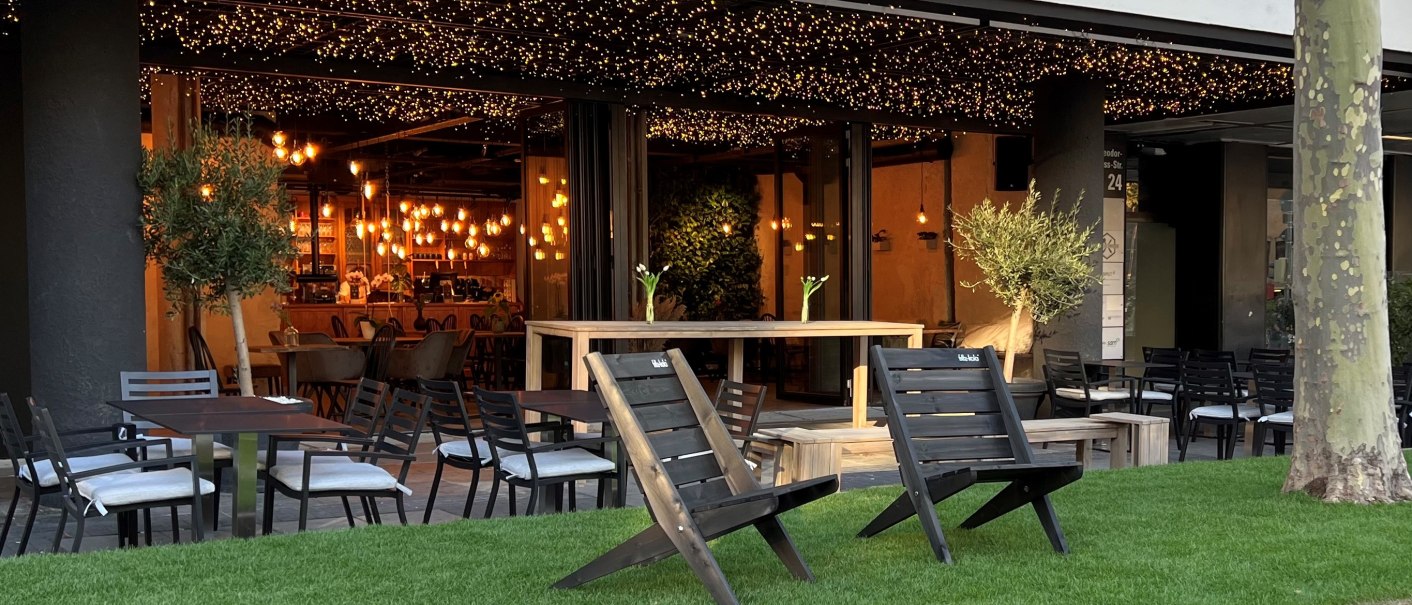 Cozy outdoor area of a caf&eacute; with tables, chairs and fairy lights. The bar can be seen in the background, surrounded by warm light., &copy; heavenskitchen