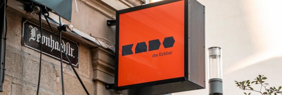 Ein leuchtend oranges Schild mit der Aufschrift 'Kado die Eckbar' hängt an einer Hauswand in der Leonhardstraße., © Stuttgart-Marketing GmbH, Sarah Schmid Ein leuchtend oranges Schild mit der Aufschrift 'Kado die Eckbar' hängt an einer Hauswand in der Leonhardstraße., © Stuttgart-Marketing GmbH, Sarah Schmid