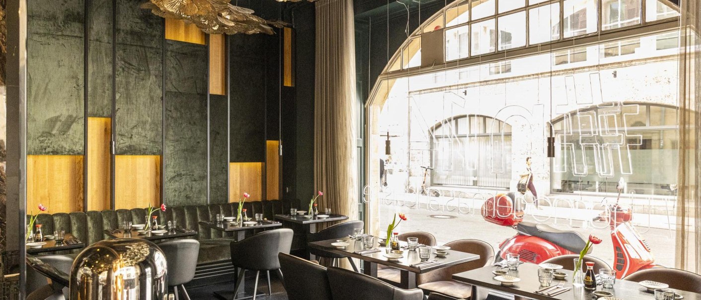 Elegantes Restaurant mit modernen Möbeln, großen Fenstern und stilvoller Dekoration. Draußen sind rote Motorroller zu sehen., © Stuttgart-Marketing GmbH, Sarah Schmid