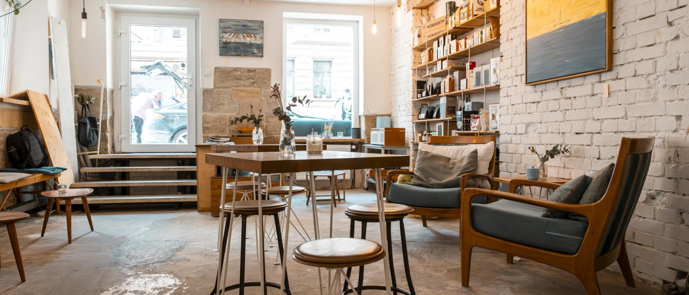 Gemütliches Café mit Holzmöbeln, weißen Backsteinwänden und Regalen. Große Fenster lassen viel Licht herein. Einladende Atmosphäre mit Pflanzen und Dekoration., © Stuttgart-Marketing GmbH, Sarah Schmid