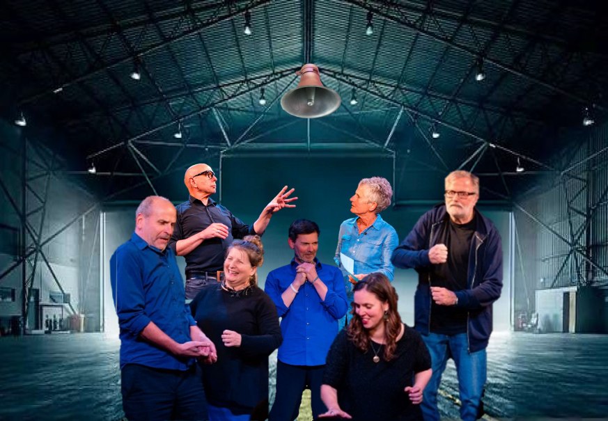 Sieben Personen einer Improtheatergruppe agieren lebhaft in einer großen, leeren Halle mit Stahlträgern und Beleuchtung., © Veranstalter Sieben Personen einer Improtheatergruppe agieren lebhaft in einer großen, leeren Halle mit Stahlträgern und Beleuchtung., © Veranstalter